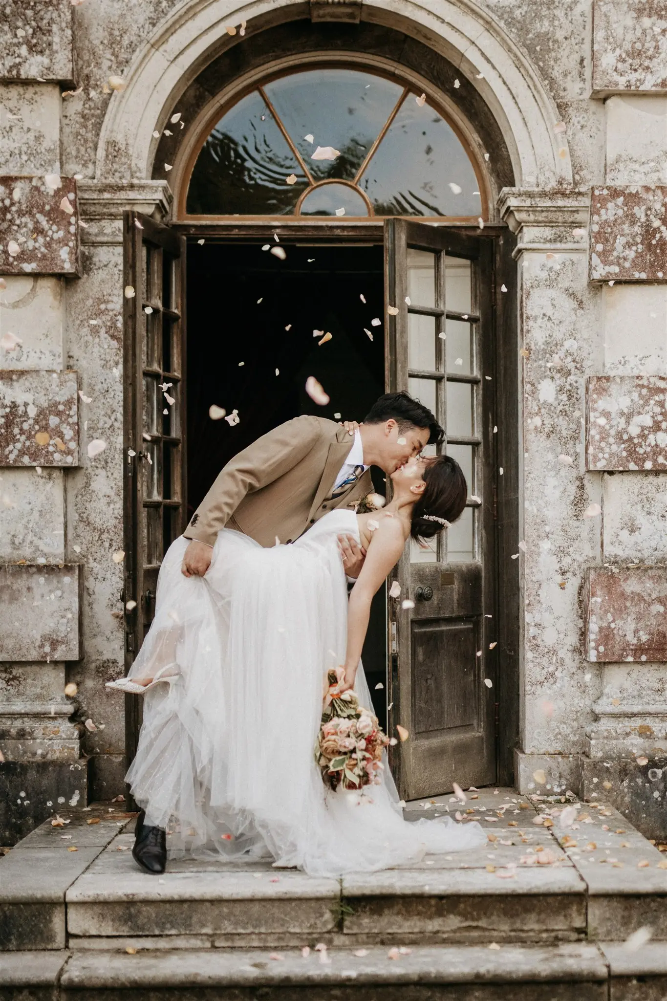 Dip kiss in stone doorway with rose petal confetti